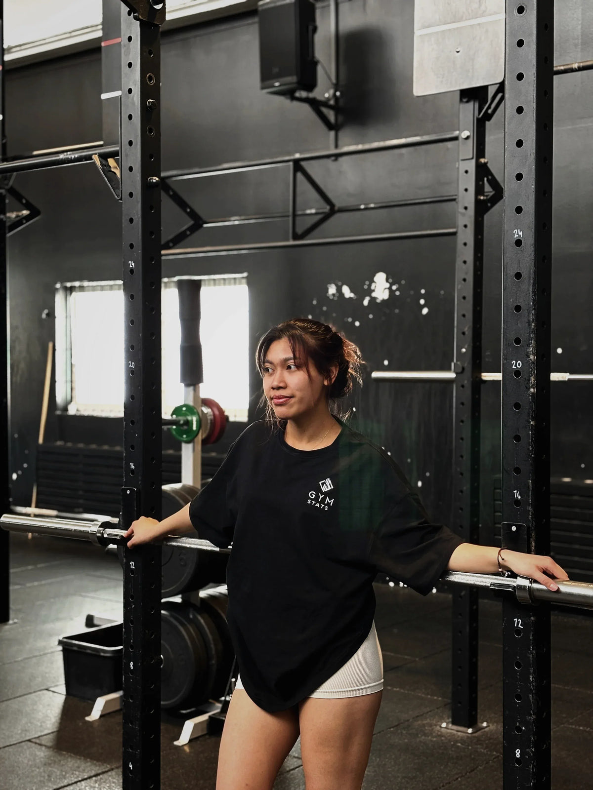 Kvinna bärande en svart, oversized Gym Stats Origin T-shirt i en gymmiljö.